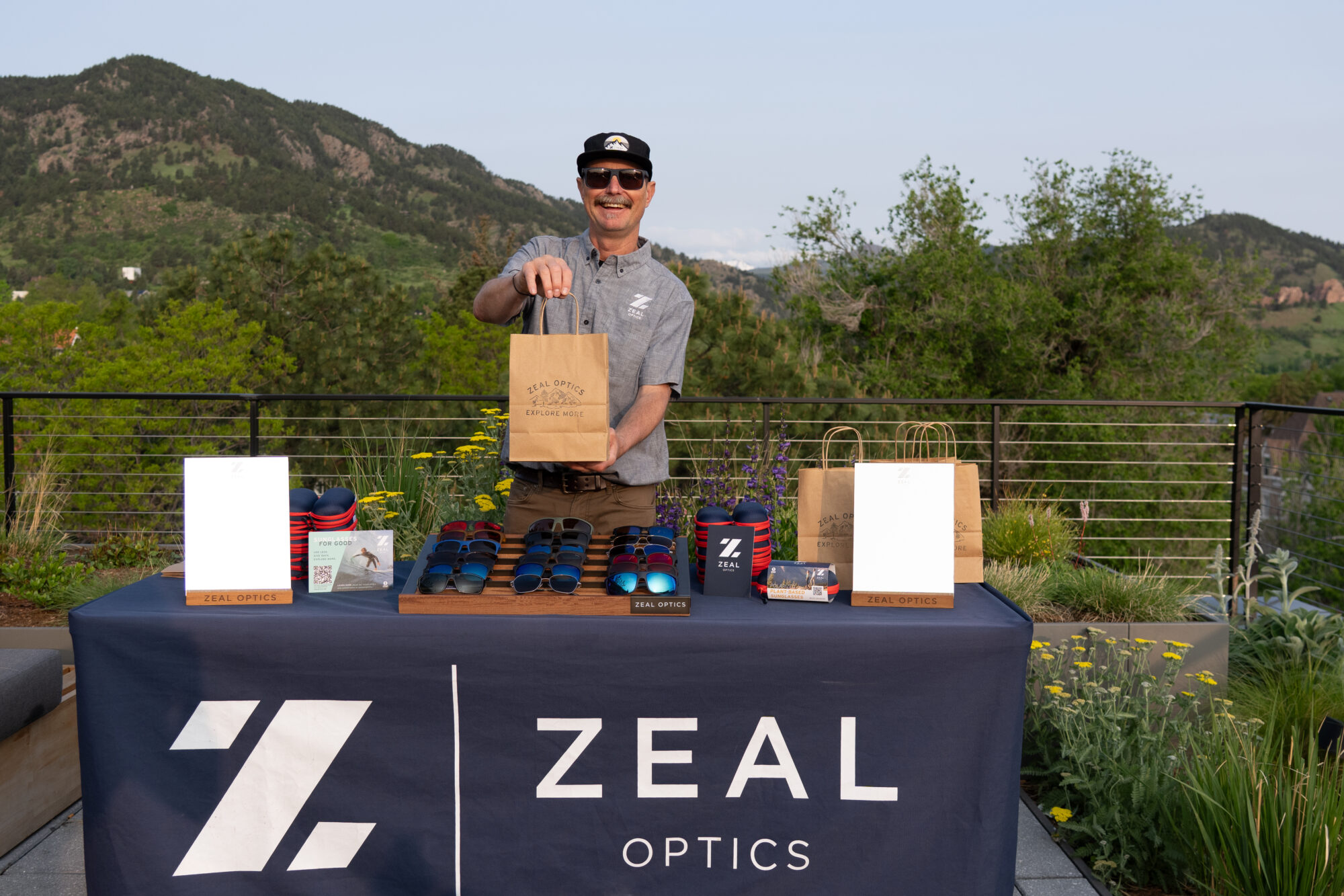man holding bag in front of table of Zeal sunglasses